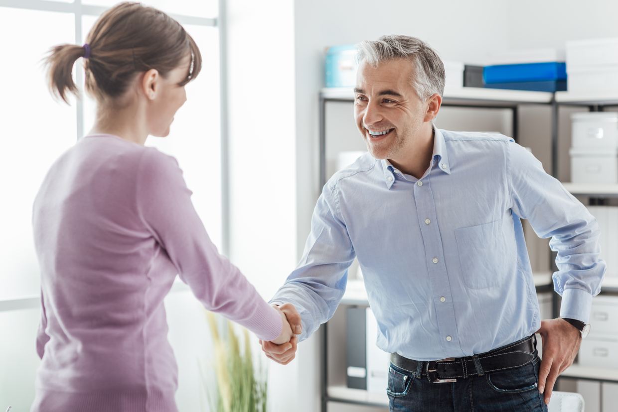 An employer welcoming a new candidate with a handshake in an office
